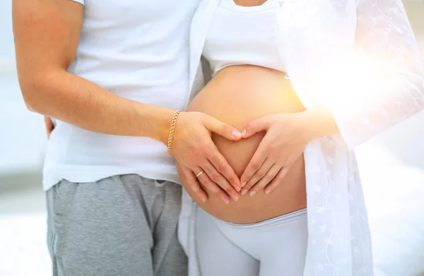 Marido e mulher grávida com as mãos dobradas na forma de um coração em sua barriga — Fotografia de Stock