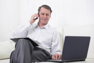 laptop ile çalışan ve bir cep telefonuyla konuşan işadamı