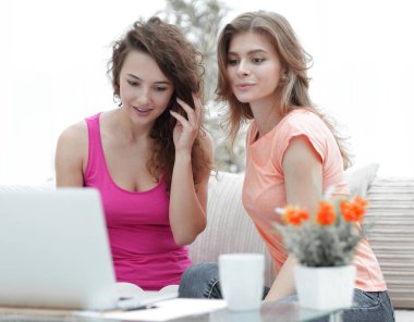 iki öğrenci kız kanepede otururken dizüstü bilgisayar ekranına bakarak.