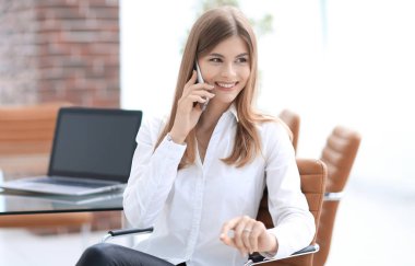 Ofiste oturan iş kadını cep telefonuyla konuşuyor.