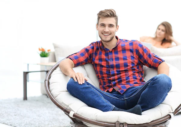 Joven moderno sentado en una gran silla redonda sobre fondo borroso — Foto de Stock