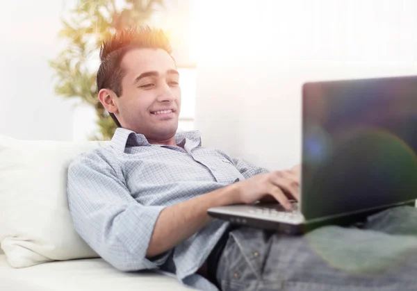 Jovem, homem bonito usando laptop sentado no sofá — Fotografia de Stock