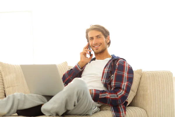 Серьезный молодой человек с ноутбуком разговаривает по мобильному телефону — стоковое фото