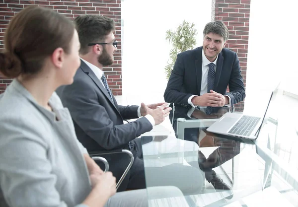 Gerente positivo com sua equipe sentada na mesa — Fotografia de Stock