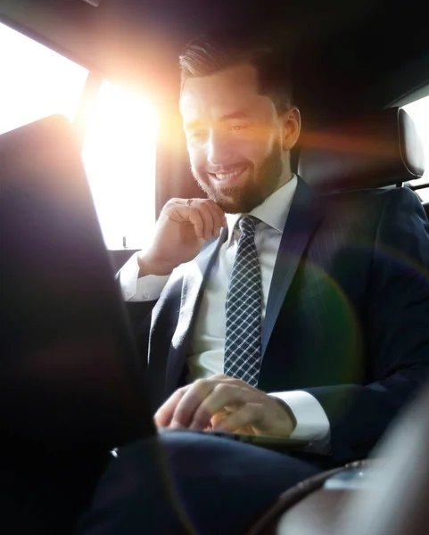 Caucasian male business executive travelling by a car and working on laptop computer. — Stock Photo, Image