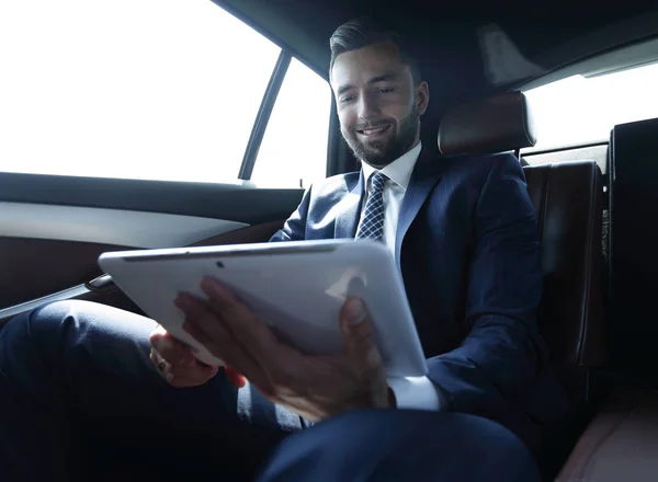 Uomo d'affari che lavora sul sedile posteriore di un'auto e utilizza un tablet — Foto Stock