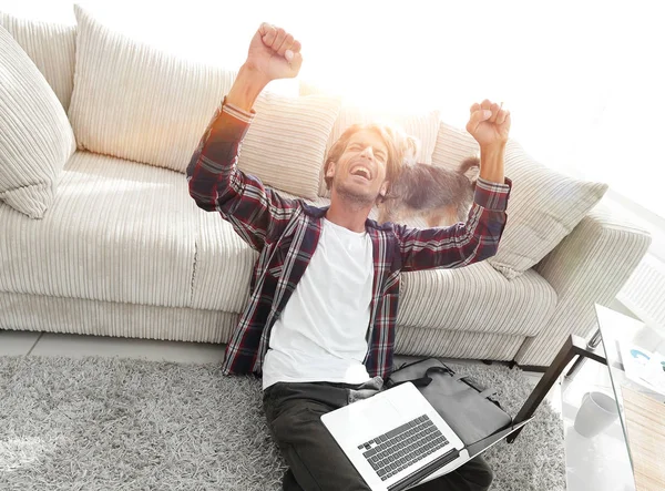 Cara feliz com laptop jubilante na espaçosa sala de estar . — Fotografia de Stock