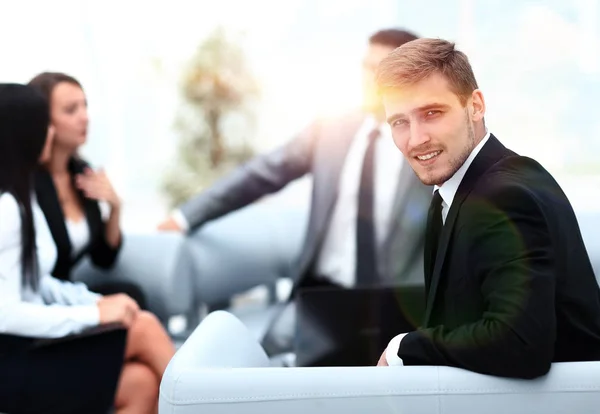 Erfolgreicher gutaussehender Geschäftsmann sitzt am Schreibtisch vor verschwommenem Hintergrund — Stockfoto