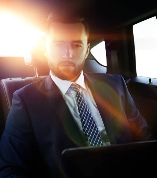 Businessman with laptop sitting in a comfortable car — Stock Photo, Image