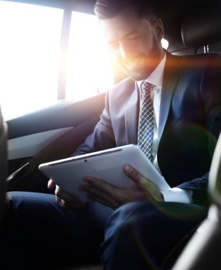 bir arabanın arka koltuğunda oturan bir dijital tablet ile işadamı