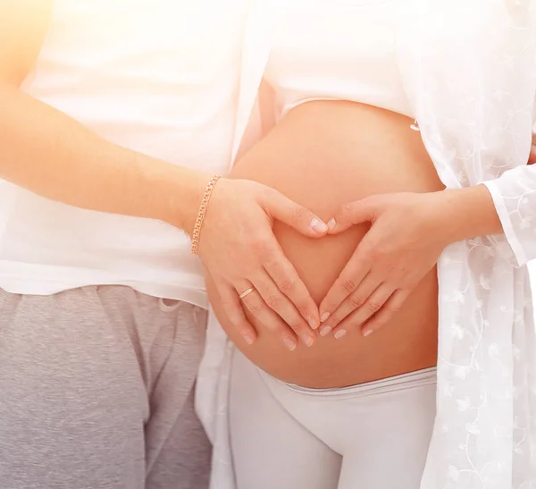 Husband and pregnant wife with folded hands in the shape of a heart on his tummy — Stock Photo, Image