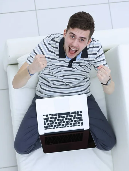 Vista de cima. jovem jubiloso com laptop sentado no sofá — Fotografia de Stock