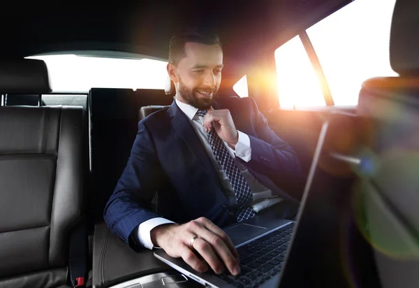 Uomo d'affari legge le informazioni sul computer portatile mentre seduto in auto — Foto Stock