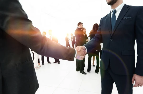 Крупный план рукопожатия деловых партнеров на фоне деловой команды — стоковое фото