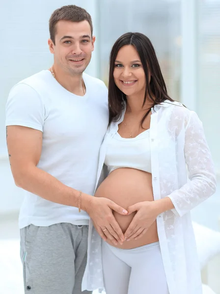 Man en zwangere vrouw met gevouwen handen in de vorm van een hart op zijn buik — Stockfoto