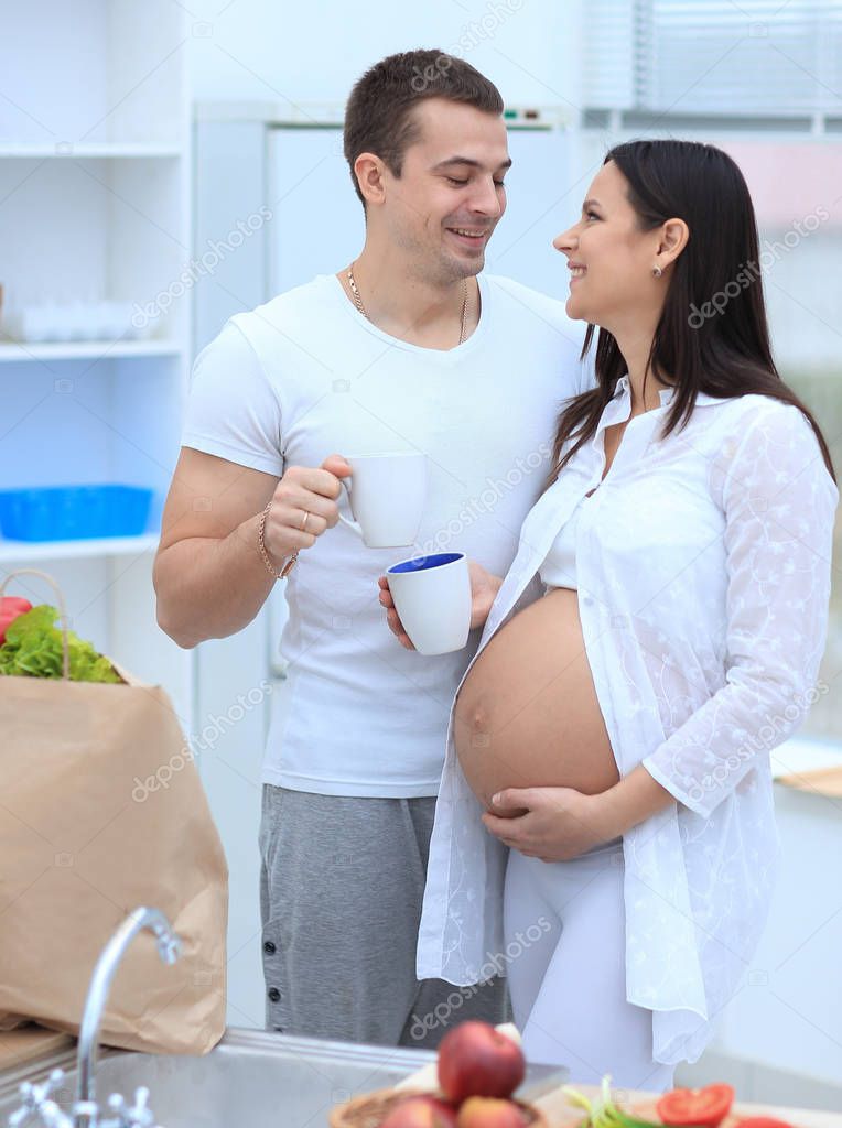 marido y su esposa embarazada bebiendo cacao, de pie en la cocina. 2023