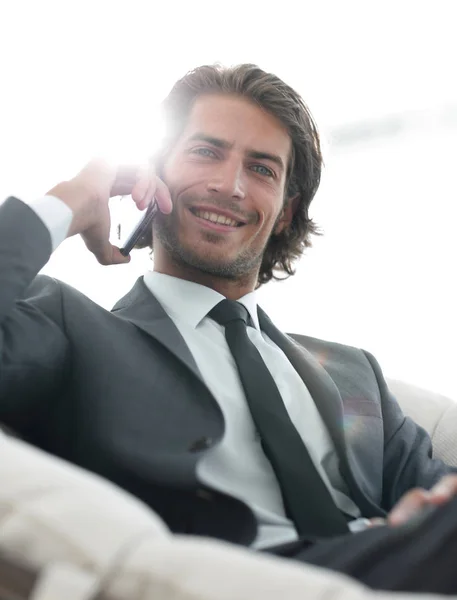 Hombre de negocios hablando en un teléfono inteligente mientras está sentado en una silla cómoda . — Foto de Stock