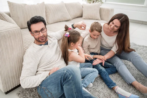 Família feliz sentado no tapete na sala de estar — Fotografia de Stock