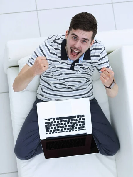 Widok z góry. uradowany młody człowiek z laptopa siedząc na kanapie — Zdjęcie stockowe