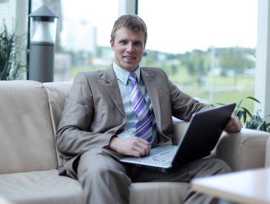 Laptop ile çalışma ofis lobisinde oturan genç işadamı