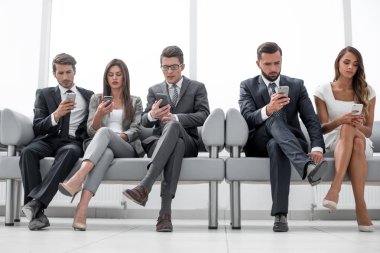 Ofis koridorunda oturan akıllı telefonlu iş arkadaşları.