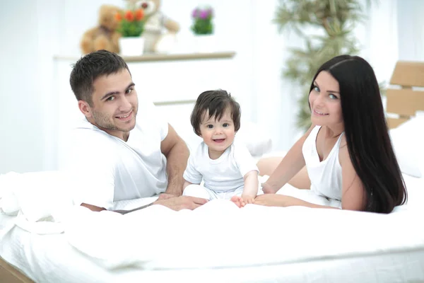 Happy young family with a baby lying in bed and smiling — Stock Photo, Image
