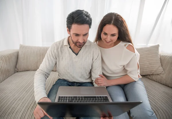 Couple with laptop sitting in the living room on the sofa — Stock Photo, Image