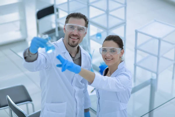 Cientista e assistente olhar para o líquido no frasco — Fotografia de Stock