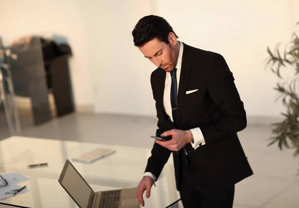 Homme d'affaires lisant un message texte sur smartphone, debout au bureau — Photo