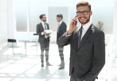 Banka ofisinin yanında cep telefonu olan bir işadamı duruyor.
