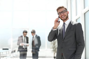Banka ofisinin yanında cep telefonu olan bir işadamı duruyor.