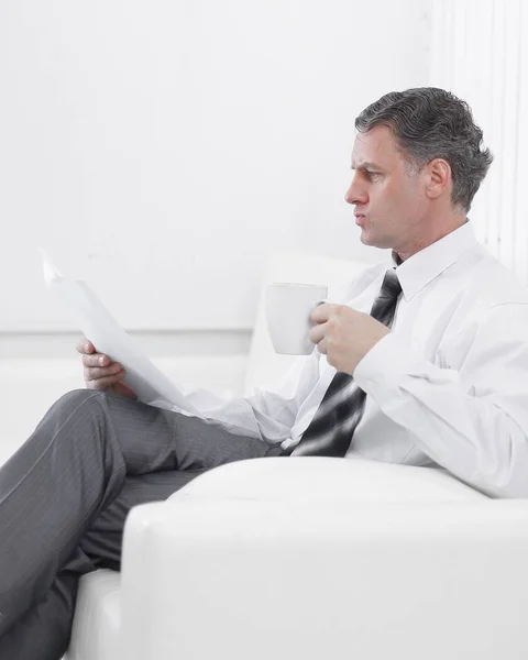 Affärsman som läser ett dokument medan du sitter i en stol på hotellrummet. — Stockfoto