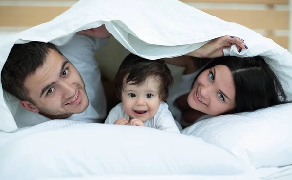 Família feliz posando sob um edredom enquanto olha para a câmera — Fotografia de Stock