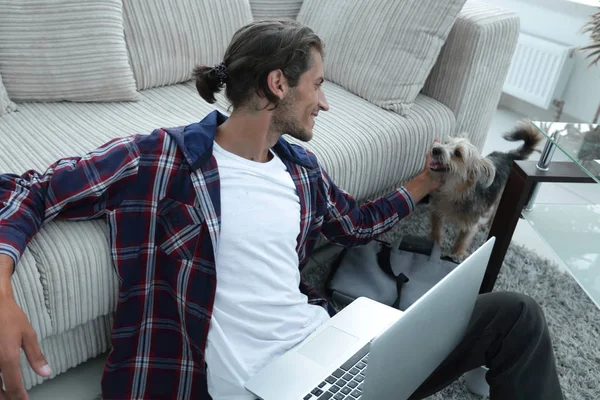 Elegante giovane uomo accarezzando il suo animale domestico e lavorando sul computer portatile — Foto Stock