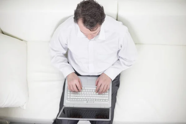 Vista desde el top.man trabajando en el ordenador portátil tumbado en un sofá . —  Fotos de Stock