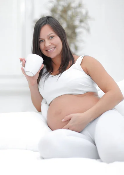 Glad gravid kvinna konsumtionsmjölk som sitter i vardagsrummet. — Stockfoto