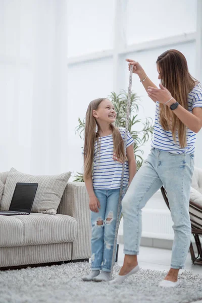 Mujer joven midiendo la altura de sus hijas en casa —  Fotos de Stock