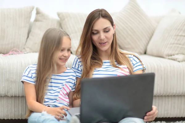 Mãe e filha deitado sentado na sala de estar e usando um laptop — Fotografia de Stock