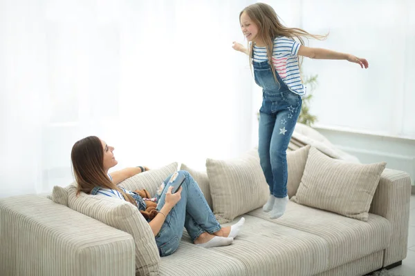 Mamá y su hija pequeña están jugando en el sofá en la sala de estar —  Fotos de Stock