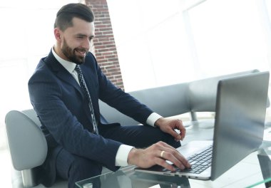 ofis lobisinde otururken dizüstü bilgisayar üzerinde çalışan iş adamı