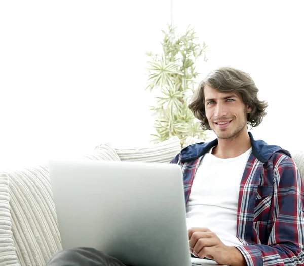 Portret van een jonge man met een laptop die zittend in een stoel — Stockfoto