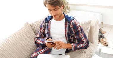 dizüstü bilgisayar ve akıllı telefon oturma odasında ciddi genç adam.