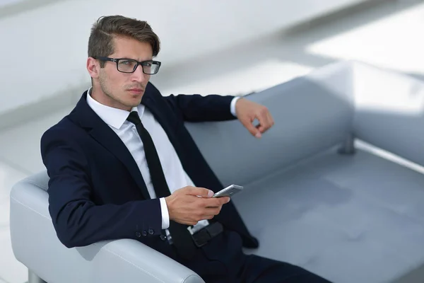 Homme d'affaires sérieux avec mobile assis dans le hall du bureau — Photo