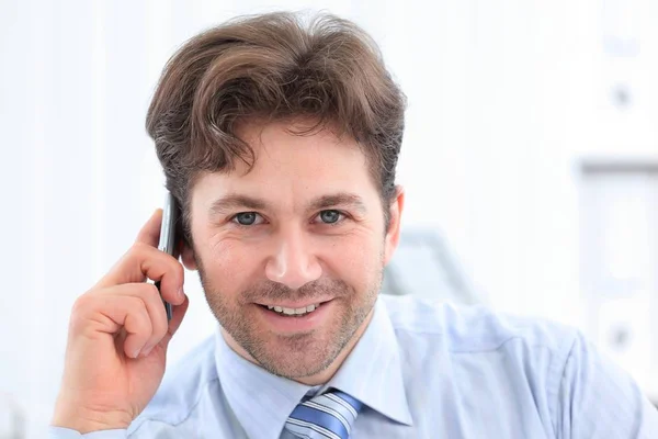 Bonito empresário sentado na mesa e falando em um telefone celular — Fotografia de Stock