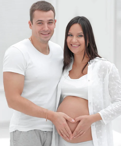 Marito e moglie incinta con le mani incrociate a forma di cuore sulla pancia — Foto Stock