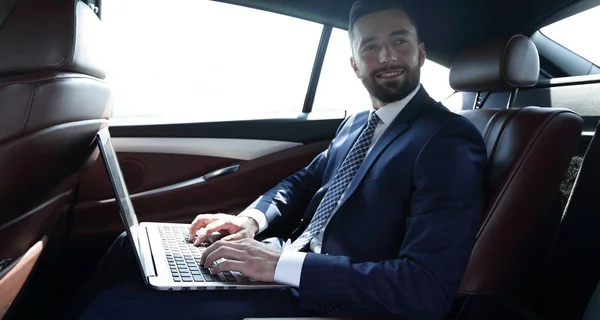 Hombre de negocios con portátil sentado en el asiento trasero de un coche —  Fotos de Stock