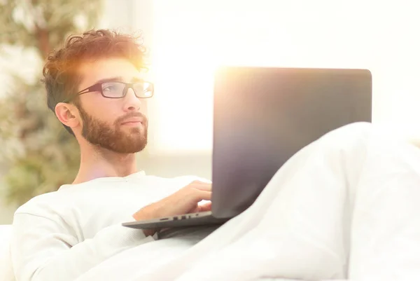 Homem bonito trabalhando no laptop deitado na cama — Fotografia de Stock