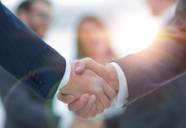 Two businessmen shaking hands with colleagues  on background.