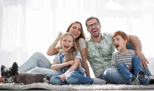 Веселая семья сидит на ковре в новой гостиной — стоковое фото