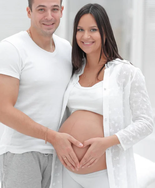 丈夫和怀孕的妻子，双手交叉，肚子上有一颗心的形状 — 图库照片
